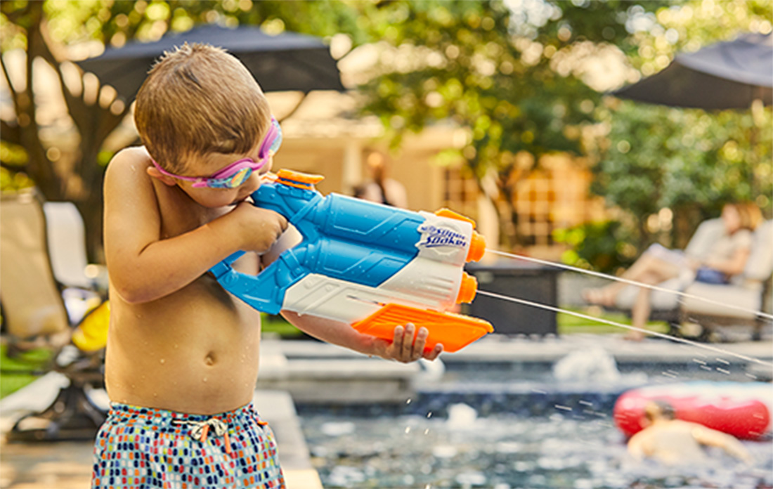happy boy playing poolside with water pistol and swim goggles.